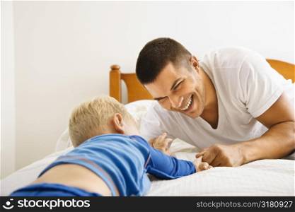 Caucasian toddler boy and father playing in bed.