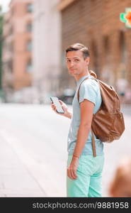 Caucasian tourist with smartphone in hands walking along the deserted italian streets in Rome. Young urban boy on vacation exploring european city. Boy caucasian with smartphone walking in street at Europe