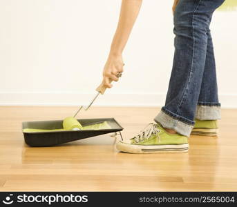 Caucasian woman dipping paint roller in tray of paint.