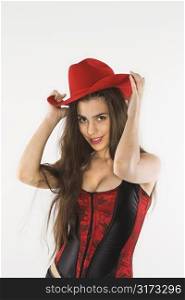 Caucasian woman in corset with hand on top of red cowboy hat.