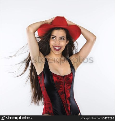 Caucasian woman in corset with hand on top of red cowboy hat.
