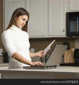 Caucasian woman in kitchen looking at laptop computer.