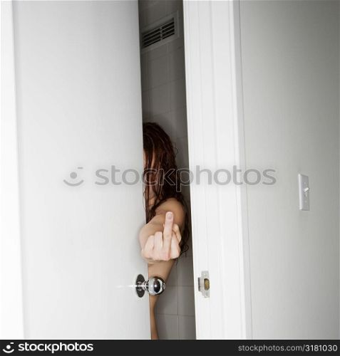 Caucasian woman in partially opened door making vulgar gesture at viewer.