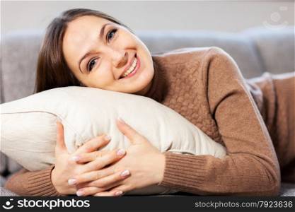 Caucasian woman is smiling towards the camera while hugging a pillow