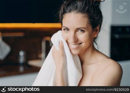 Caucasian woman is wiping face with towel after washing and smiling. Young woman takes shower at home and doing daily skin care. Hygiene and wellness, dermatology and skin cleansing.. Caucasian woman is wiping face with towel and smiling. Hygiene, dermatology and skin cleansing.