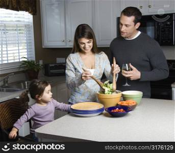 Caucasian woman making salad on kitchen counter with daughter and husband.