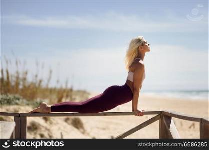Caucasian woman practicing yoga at seashore. Young female on wooden bridge, Andalusia, Spain.. Caucasian blonde woman practicing yoga in the beach