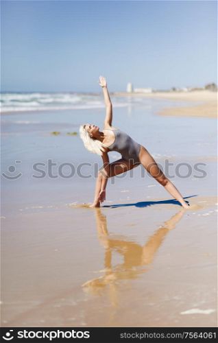 Caucasian woman practicing yoga at seashore. Young female raising arms in the beach in Cadiz, Andalusia, Spain.. Caucasian blonde woman practicing yoga in the beach