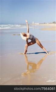 Caucasian woman practicing yoga at seashore. Young female raising arms in the beach in Cadiz, Andalusia, Spain.. Caucasian blonde woman practicing yoga in the beach