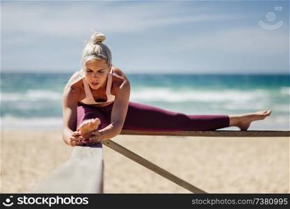 Caucasian woman practicing yoga at seashore. Young female stretching legs in the beach in Cadiz, Andalusia, Spain.. Caucasian blonde woman practicing yoga in the beach