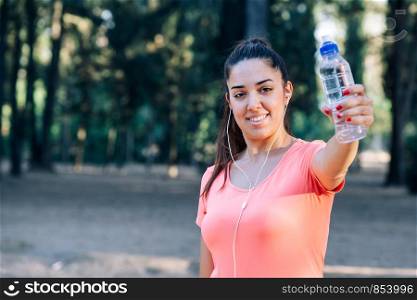 Caucasian woman showing bottle of water and listening to music while exercising.