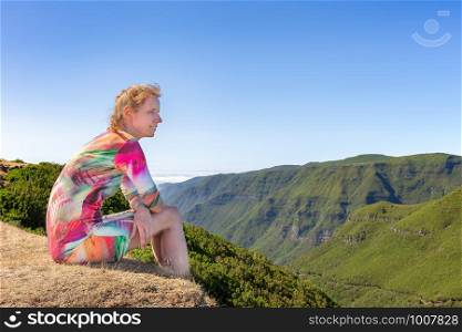 Caucasian woman sits on portuguese mountain near green valley