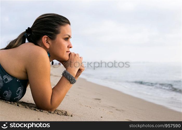 Caucasian woman wearing bikini and jewelry - bracelet - relaxing on beach. Model lying down on sand on vacation travel