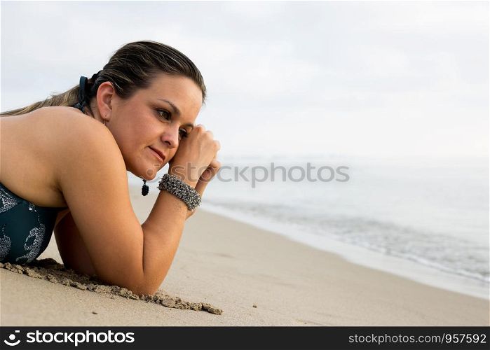 Caucasian woman wearing bikini and jewelry - bracelet - relaxing on beach. Model lying down on sand on vacation travel