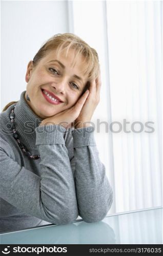 Caucasian woman with head resting on hand smiling at viewer.