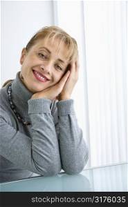 Caucasian woman with head resting on hand smiling at viewer.