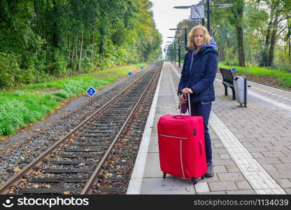 Caucasian woman with red suitcase standing on railway station