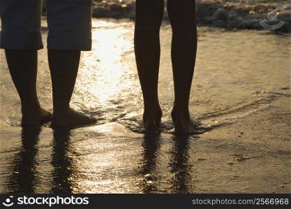 Caucasian women standing barefoot on beach in water.