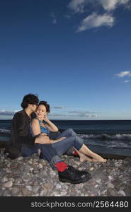 Caucasian young adult couple sitting close on beach.