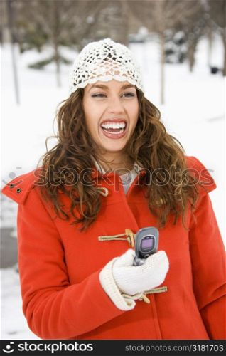 Caucasian young adult female holding cell phone and laughing in snowy climate.