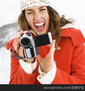 Caucasian young adult female in winter clothing pointing digital camera at viewer and winking.