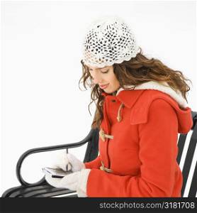 Caucasian young adult female in winter clothing sitting using PDA.