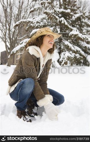 Caucasian young adult female kneeling in the snow wearing straw cowboy hat and smiling.