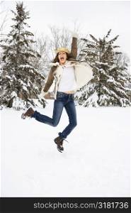 Caucasian young adult female leaping into the air in snowly climate wearing straw cowboy hat.