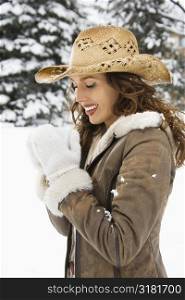 Caucasian young adult female outdoors in snow holding coffee cup and wearing straw cowboy hat.
