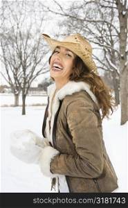 Caucasian young adult female smiling at viewer while holding snowball and wearing straw cowboy hat.