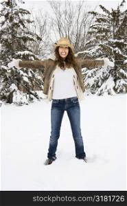 Caucasian young adult female standing with arms outstretched in snow wearing straw cowboy hat.