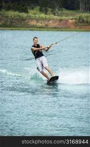 Caucasian young adult male wakeboarding on lake.