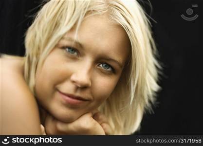 Caucasian young adult nude woman resting chin on hands and smiling at viewer.