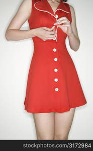 Caucasian young adult woman buttoning retro dress.