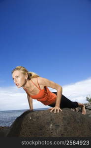 Caucasian young adult woman doing push up on rock.