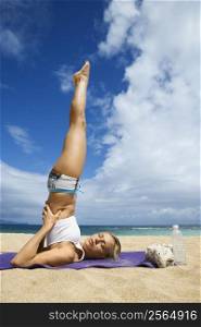 Caucasian young adult woman doing yoga on beach.
