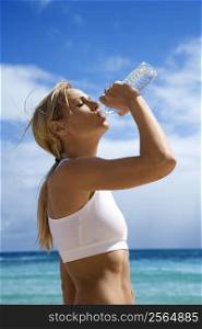 Caucasian young adult woman drinking water on beach.
