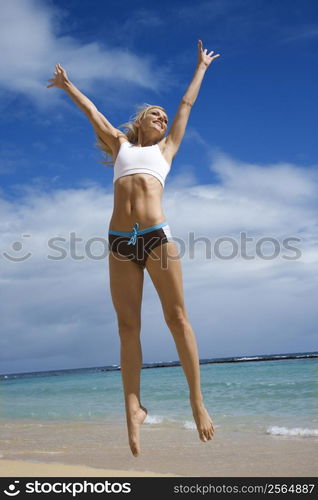 Caucasian young adult woman jumping on beach.