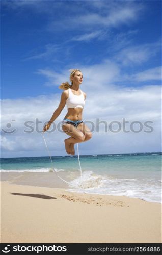Caucasian young adult woman jumping rope on beach.
