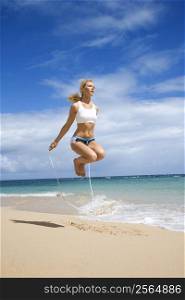 Caucasian young adult woman jumping rope on beach.