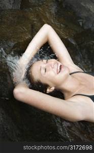 Caucasian young adult woman laying in freshwater stream laughing with arms over head.