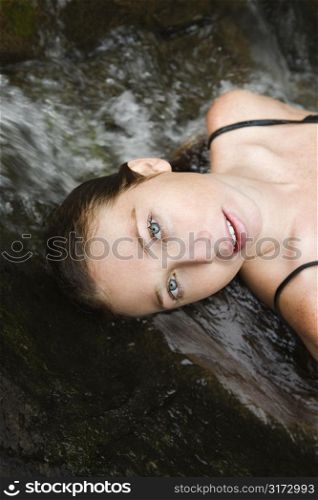 Caucasian young adult woman laying in freshwater stream looking at viewer.