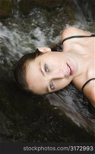 Caucasian young adult woman laying in freshwater stream looking at viewer.