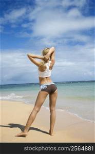 Caucasian young adult woman stretching on beach.