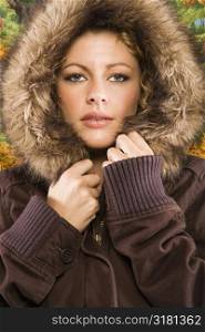 Caucasian young adult woman wearing coat with fur hood looking at viewer.