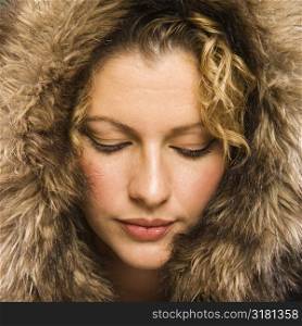 Caucasian young adult woman wearing fur hood with eyes closed.