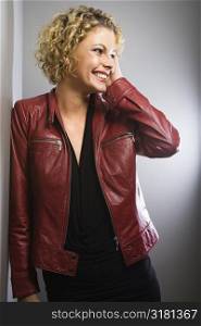 Caucasian young adult woman wearing red jacket smiling with hand to face.