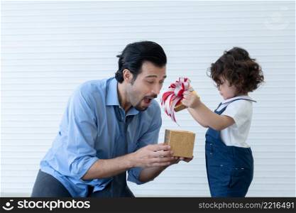 Caucasian young dad with beard and little daughter opening gift box with exciting or surprising face. Family sitting in living room at home celebrating father day or birthday special occasion