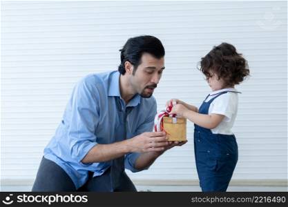 Caucasian young dad with beard smiling giving gift box to little cute daughter. Family sitting in living room at home celebrating father day or birthday special occasion