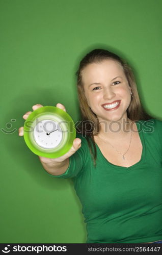 Caucasian young female adult holding out clock and smiling.